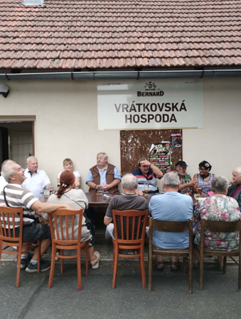 Sousedé sedí u stolů před Vrátkovskou hospodou